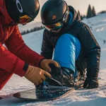 Cours de snowboard Manigod : moniteur ESF aide un élève sur la neige
